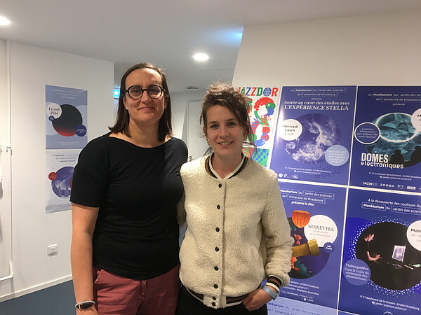 Milène Wendling, responsable du Planétarium, et Nina Pollard, chargée de communication du Jardin des sciences, devant certaines des affiches des événements organisés au Planétarium en 2024-2025. © EC