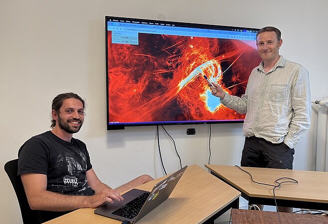 Matthieu Baumann et Laurent Chemin devant une image du centre de la voie lactée observée par le radiotélescope MeerKAT, précurseur de SKAO en Afrique du Sud. ©MR